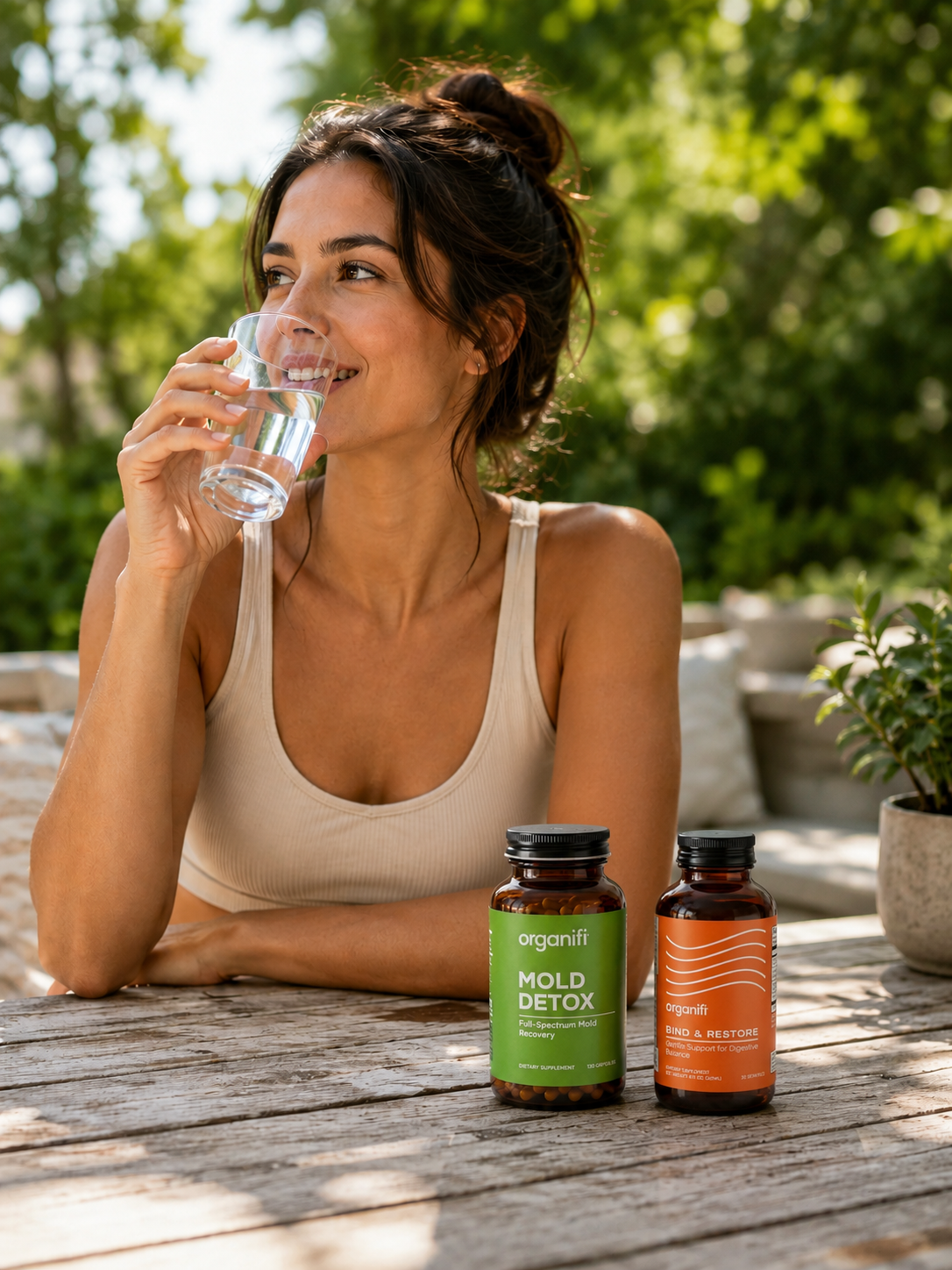 Woman with Organifi Mold Detox and Bind & Restore bottles in kitchen